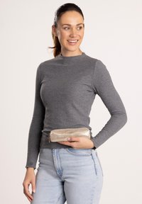 Graues, geripptes Langarmoberteil kombiniert mit hellblauen Jeans, hält eine metallisch goldene Reißverschlusstasche mit subtiler Textur und Logo.