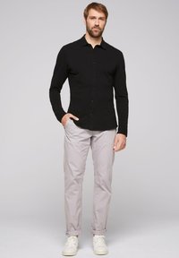 Zwarte longsleeve overhemd met een button-down kraag, gladde textuur, gecombineerd met lichtgrijze broek en witte sneakers.