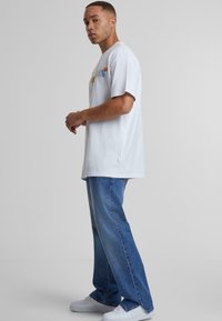 Camiseta de algodón blanca con gráfico colorido en el pecho, combinada con jeans rectos de un azul claro y zapatillas blancas. Diseño simple y casual.