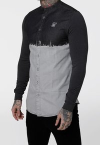 Camicia a maniche lunghe con chiusura a bottoni, caratterizzata da un upper in denim nero e un lower in tessuto grigio. Corpo testurizzato con un sottile effetto sfumato.
