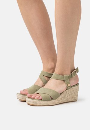Sandalias de cuña de ante verde con correas entrecruzadas, hebilla ajustable en el tobillo y detalle de yute trenzado en la suela para mayor textura.
