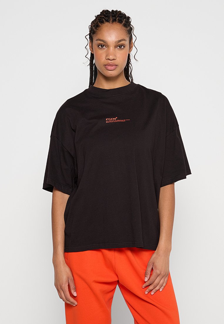 T-shirt noir surdimensionné en coton, avec un petit logo rouge sur la poitrine. Manches courtes et coupe décontractée, avec un col rond.