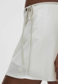 Bermudas deportivas blancas con cintura ajustable mediante cordón, textura suave y un pequeño logo en el dobladillo. Fabricadas con un tejido ligero que absorbe la humedad.