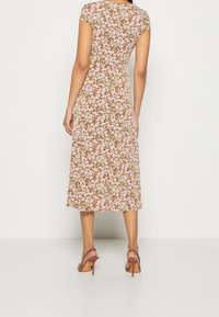 Robe midi fleurie à manches courtes, avec un fond marron et des fleurs roses. Tissu fluide tombant jusqu'au milieu du mollet. Portée avec des sandales à talons hauts.