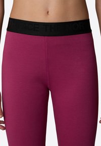 Leggings aderenti in tessuto rosa scuro con una ampia cintura elastica nera che presenta il logo "THE NORTH FACE". Texture liscia, senza motivi visibili.