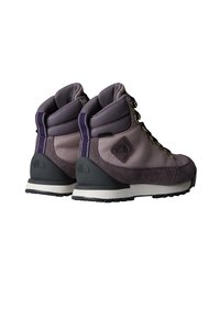 Botas de senderismo de caña alta que presentan una combinación de materiales lisos y de ante en color púrpura, suelas de goma negra duraderas y ojales metálicos amarillos.
