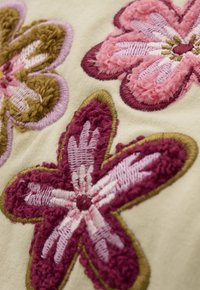 Wyhaftowany floralny wzór z różowymi, burgundowymi i oliwkowymi nitkami na kremowym tle. Teksturowane płatki z konturowymi detalami.