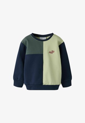 Väriblokkinen collegepaita laivastonsinisellä, vihreällä ja vaaleankeltaisella. Varustettu resorikäänteillä ja kauluksella, joissa punainen kirjailu "Club House".