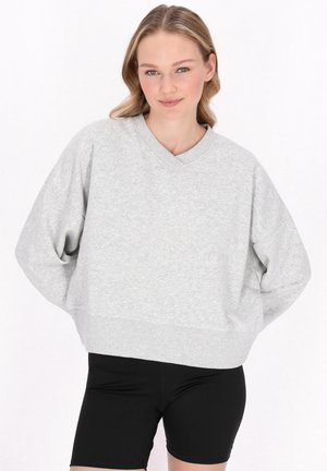 Sweatshirt court gris clair avec un col en V, des épaules tombantes et un ourlet côtelé. Accompagné de shorts noirs ajustés. Tissu doux et décontracté.