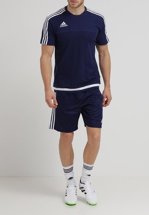 Granatowy strój sportowy składający się z koszulki z krótkim rękawem z białymi paskami, pasujących szortów oraz piłkarskich korków z zielonymi akcentami.