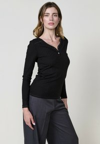 Top noir à manches longues et côtes avec un col henley et trois boutons métalliques, associé à un pantalon gris à jambes larges. Texture lisse, design ajusté.