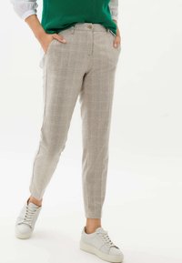 Pantalon à carreaux gris clair avec une coupe ajustée, poches latérales et une texture lisse, associé à des baskets blanches.