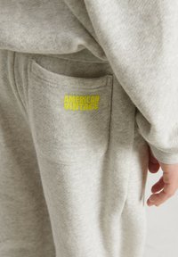 Svetlošedý materiál mikiny s malou kapsou a jasne žltým logom "AMERICAN VINTAGE". Mäkkučký povrch, ležérny dizajn.