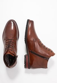 Bottines en cuir marron avec bouts ronds, lacets à l'avant et fermeture éclair sur le côté. Surface texturée, talon légèrement rehaussé et semelle en caoutchouc.