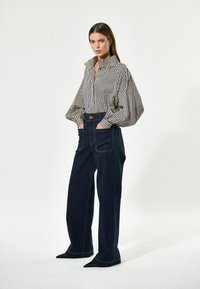 Gestreifte Hemdbluse mit hohem Kragen, kombiniert mit hochtaillierten dunklen Jeans mit Fronttaschen und kontrastierenden Nähten.