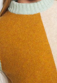 Sweter dęty z prążkowanym, miętowym dekoltem i panelami w kolorze blokowym w musztardowej żółci, beżu i jasnym brązie. Miękka tekstura.