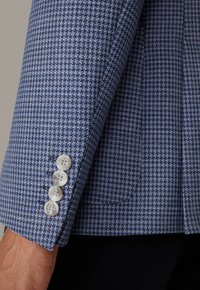 Rękaw kurtki w niebiesko-białym wzorze pepitki o gładkiej fakturze. Na mankiecie cztery okrągłe, jasne guziki.