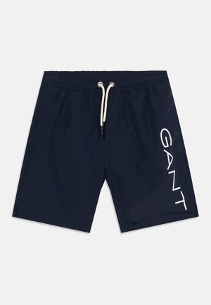 Granatowe spodenki kąpielowe z białym sznurkiem w pasie i dużym, białym logo „GANT” nadrukowanym pionowo na lewej nogawce.