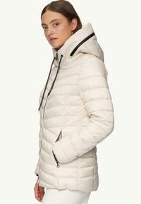 Cremefarbene Daunenjacke mit hohem Kragen, schwarzen Akzenten, Reißverschlusstaschen und einem strukturierten, gesteppten Muster.