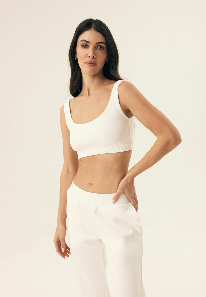 White crop top with wide straps and gathered hem paired with loose white pants featuring a subtle logo. Smooth, soft fabric and relaxed fit.