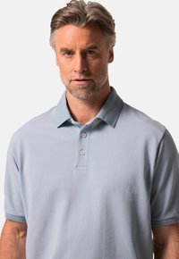 Jasnoniebieska koszulka polo z kołnierzykiem, zapięciem na dwa guziki, krótkimi rękawami i gładką fakturą. Posiada kontrastujące wykończenia kołnierzyka i rękawów.