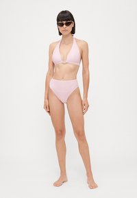 Bikini rosa a righe con top triangolare che presenta un accento circolare. Slip alto in vita. Tessuto morbido, design minimalista.