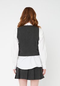 Gray pinstriped vest, fitted design with a high back, worn over a white shirt and pleated skirt. Fabric appears textured and tailored.