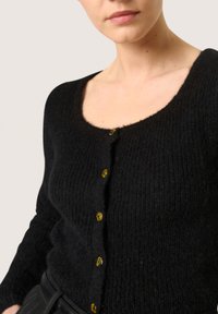 Crna cardigan jakna s rebrastom teksturom, okruglim dekolteom i žutim dugmadima, s prilagođenim krojem i dugim rukavima.