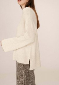 Maglione lungo a maniche, di colore crema, con orlo a coste e spacchi laterali, abbinato a una gonna grigia a fantasia con un sottile motivo animale.