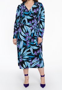 Černé zavinovací šaty s modrými listy a fialovými květinami, s dlouhými rukávy a páskem v pase. Doplněné o fialové lodičky.
