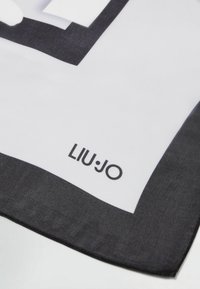 Valge siidsall musta äärisega. Omab silmapaistvat graafilist disaini ja musta "LIU JO" logot nurgas. Sile tekstuur.