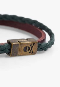 Pulsera de cuero trenzado en colores verde oscuro y burdeos, con un broche de bronce detallado con una calavera y un símbolo de "X".