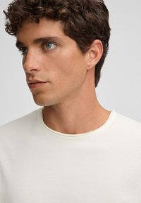 Hellbeige T-Shirt mit rundem Ausschnitt, aus weichem Stoff, mit kurzen Ärmeln und glatter, unverbauter Textur.