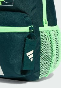 Tamnozelena ruksak s mrežastom bočnom džepom, svijetlozelenim patentnim zatvaračem i oznakom s brendom koja ima tri dijagonalne pruge u bijeloj boji.