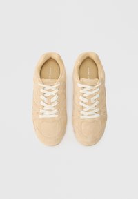 Zapatillas de ante beige con cordones blancos, que presentan una textura suave, forma redondeada y diseño minimalista. Logotipo impreso en la plantilla.
