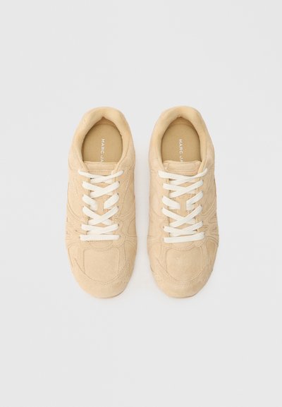 Sneakers in suede beige con lacci bianchi, caratterizzate da una texture liscia, forma arrotondata e design minimalista. Logo stampato sulla soletta.