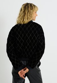 Veste bomber en velours noir avec un motif matelassé en losanges et des coutures métalliques. Équipée de poignets côtelés et d'une coupe décontractée.