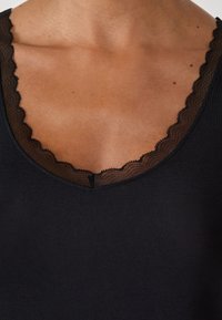 Top black senza maniche con scollatura in pizzo trasparente a forma di scallop. Il tessuto appare morbido con una texture liscia, mettendo in risalto il dettaglio del colletto.