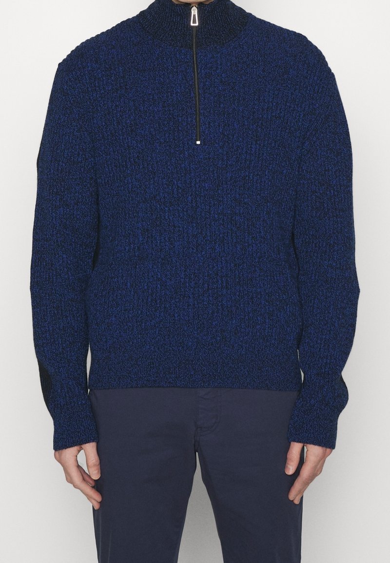 Blauer Strickpullover mit hohem Kragen, halbem Reißverschluss und langen Ärmeln, die mit strukturiertem Stoff und gerippten Bündchen versehen sind.