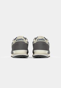 Sneaker con una combinazione di colori grigio e crema, caratterizzati da una tomaia testurizzata, dettagli perforati e una suola intermedia bianca con un battistrada in gomma nera.