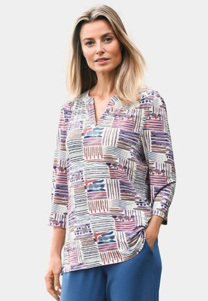 Blouse à motifs multicolores avec des manches 3/4, présentant des designs géométriques en violet, rouge et bleu sur un fond clair, avec un décolleté en V.