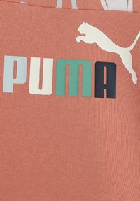 Korallivärinen t-paita, jossa on tekstuuri kangas, jossa on "PUMA"-logo vaaleanharmaana, vihreänä ja tummansinisenä, sekä valkoinen hyppäävä puma -grafiikka.