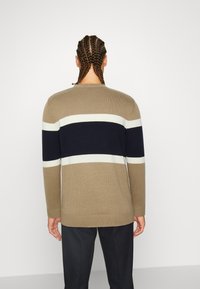 Sweter typu pulower w poziome paski w kolorach beżowym, granatowym i białym. Żebrowany dekolt i mankiety, o miękkiej fakturze i luźnym kroju.