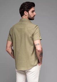Korte mouwen olijfgroen shirt met een gladde katoenstructuur, kraag, en rechte zoom, gecombineerd met lichtgekleurde broek.