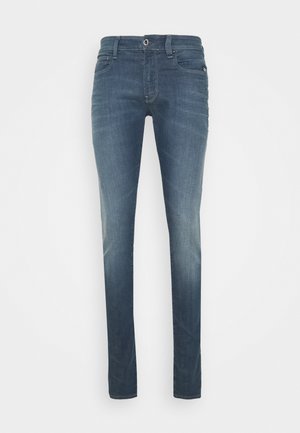 Jean slim en denim bleu avec léger délavage, style cinq poches, fermeture à boutons et passants de ceinture, présenté sur un fond blanc plat.