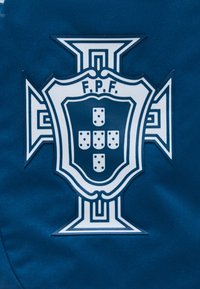 Emblème blanc avec les lettres F.P.F. et cinq petits écus disposés en croix sur un fond bleu.