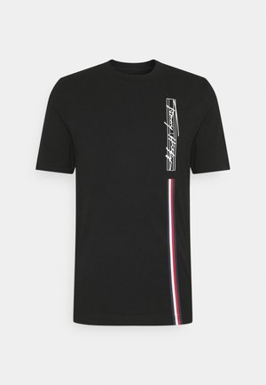 T-shirt en coton noir avec un design en art linéaire blanc sur le côté gauche et une bande verticale rouge, blanche et bleue sur le côté droit. Manches courtes.