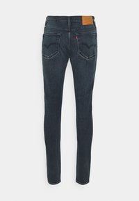 Jeans ajustados de mezclilla azul oscuro con un acabado texturizado, que cuentan con bolsillos traseros y una etiqueta de cuero marrón en la banda de la cintura.
