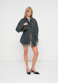 Denim oversized srajca-jakna z gumbom, položena preko mini obleke z leopardjim vzorcem. Črne slingback pete in rjava torbica dokončata videz.