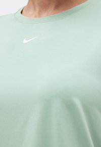 Κοντινό πλάνο ενός ατόμου που φοράει ανοιχτοπράσινο μπλουζάκι Nike με λευκό λογότυπο Nike κάτω από το λαιμόκοψη.